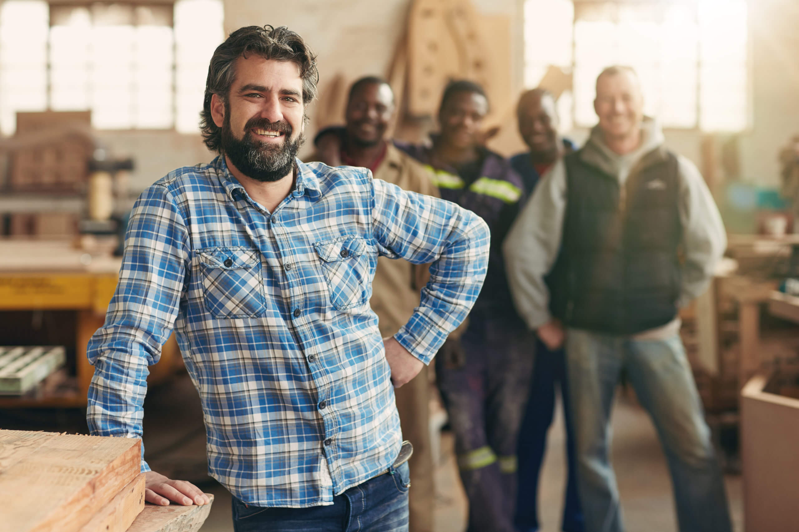 A,Smiling,Carpenter,With,His,Staff,In,The,Background