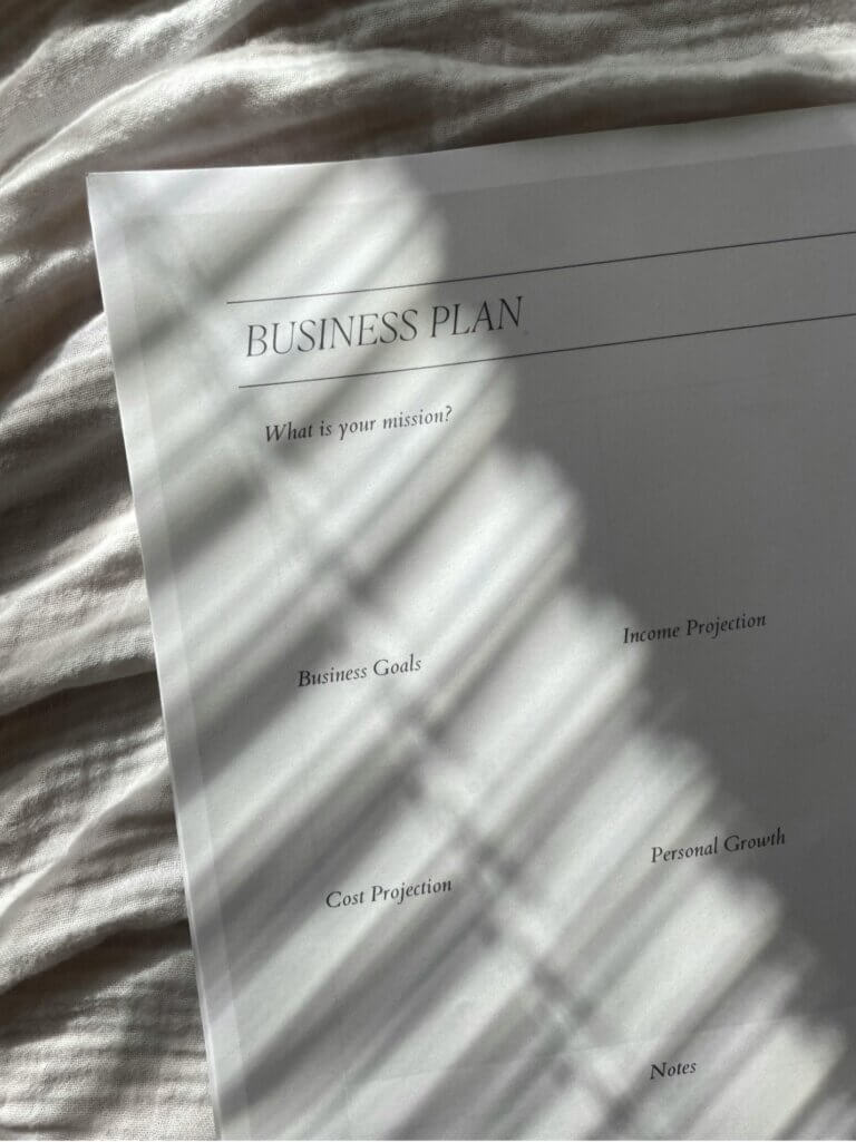 A document titled "Business Plan" outlining a business's mission, goals, finances, and personal growth aspirations rests on top of a bed.
